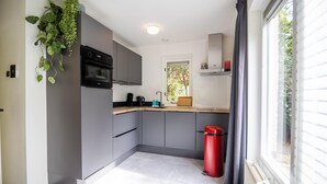 A modern kitchen with grey cabinets, a black oven, and a red trash bin.