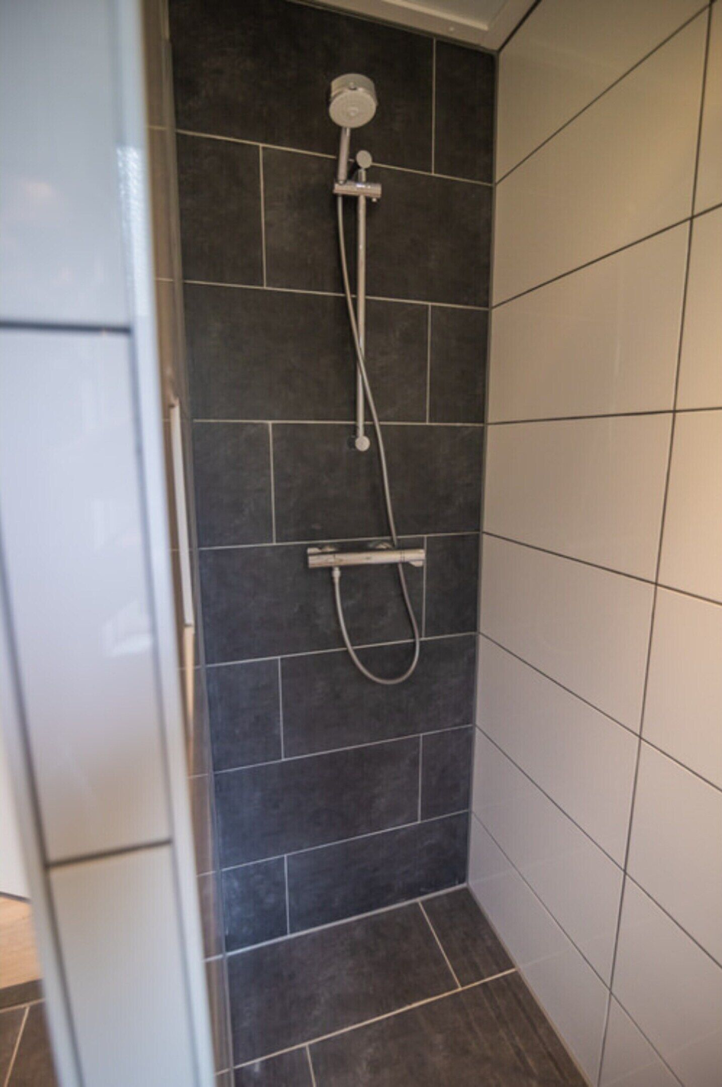 A shower area with dark tiles and a white tiled wall.