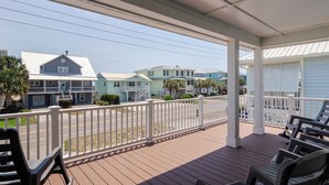 A covered porch with a white railing, wooden deck, and several chairs.