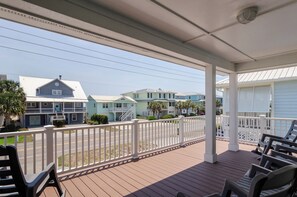 A covered porch with a white railing, wooden deck, and several chairs.