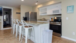 A kitchen with white cabinets, a stainless steel refrigerator, a microwave, a stove, and a granite countertop.