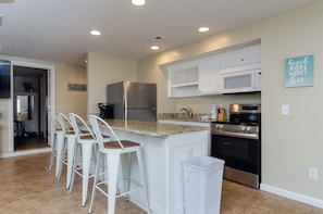 A kitchen with white cabinets, a stainless steel refrigerator, a microwave, a stove, and a granite countertop.