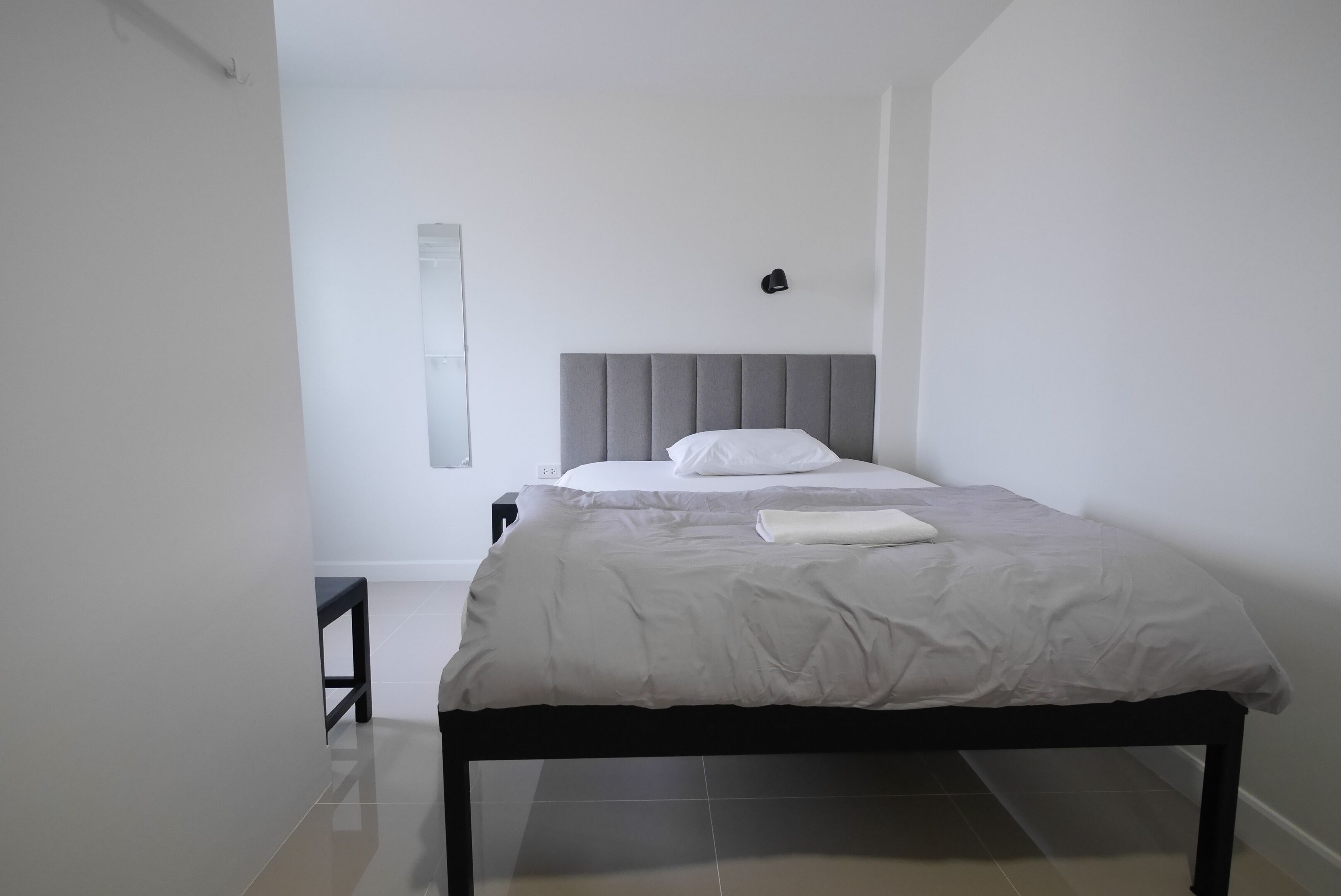 Una camera da letto moderna con una testiera grigia rivestita in tessuto, un letto rifatto con lenzuola bianche e un comodino.