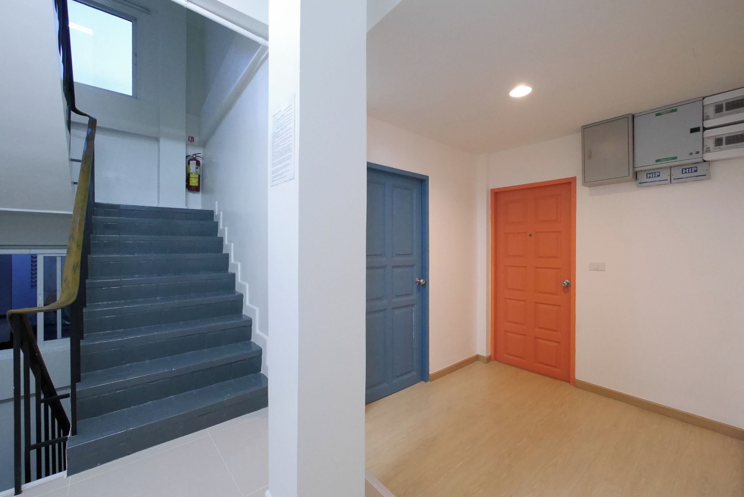 Een trap met een leuning, een blauwe deur en een oranje deur.