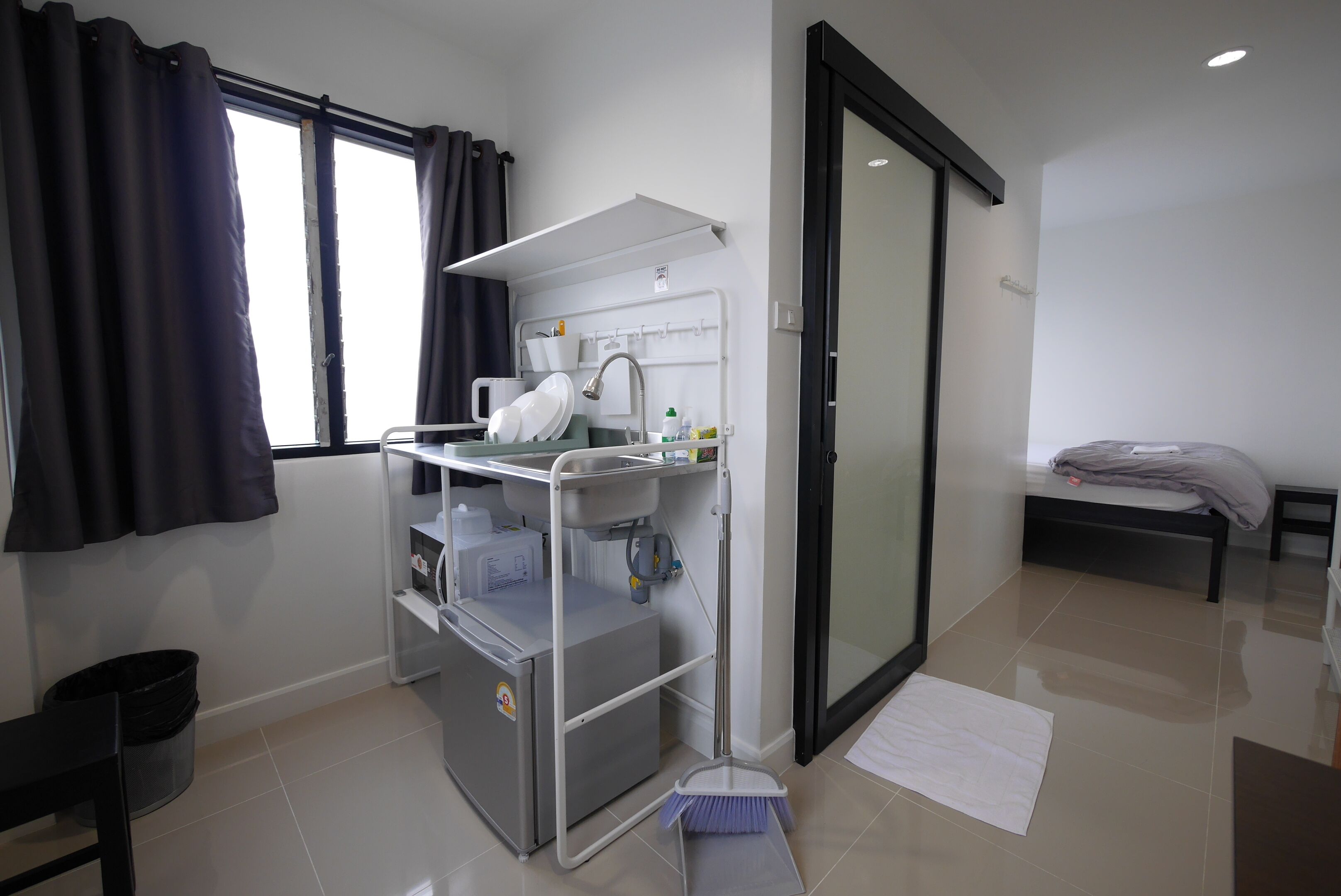 Une salle de bain moderne avec un lavabo, un miroir et un meuble de rangement. On y trouve un espace douche doté d’une porte en verre, d’un petit banc et d’une fenêtre avec des rideaux.