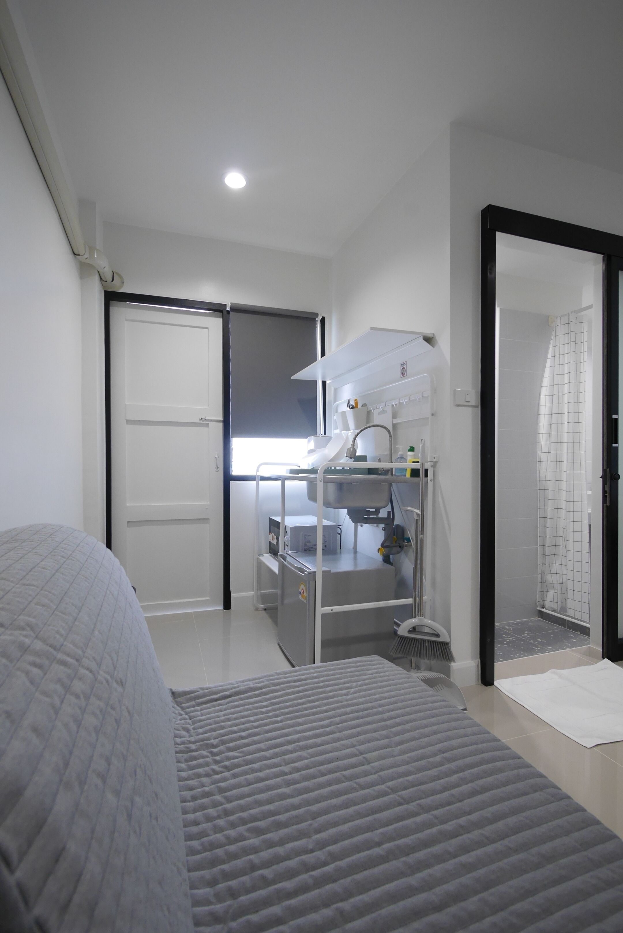 A bedroom with a bed, a bathroom with a shower, and a kitchenette area.