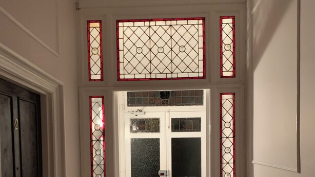 A hallway with a patterned floor, a white door with glass panels, and decorative stained glass windows.