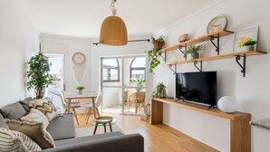 Un soggiorno moderno con divano, televisione, mensole in legno con piante e un'area pranzo con sedie e tavolo.