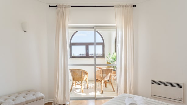 Una camera da letto con un letto, una panca, un termosifone e vista su un balcone con sedie e un tavolo.