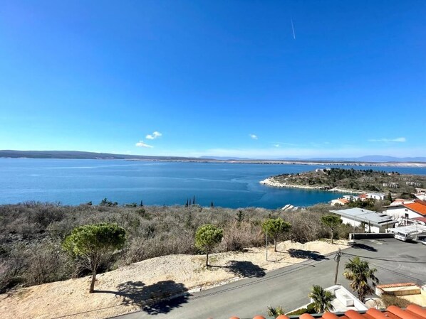 A coastal landscape with a clear view of the sea, a road, and sparse vegetation.