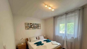 Un dormitorio con cama, mesitas de noche, una alfombra y una ventana con cortinas.