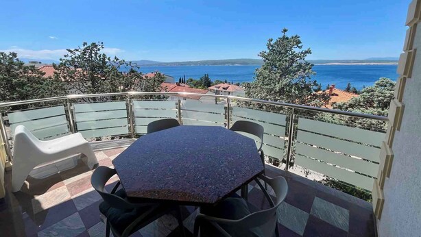 Un balcón con mesa y sillas, que ofrece vistas al mar y edificios lejanos.
