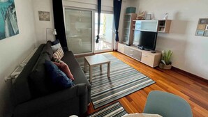 Una sala de estar con sofá, televisor y puerta corrediza de vidrio que da a un balcón.