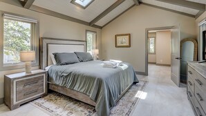 A bedroom with a bed, bedside tables, a dresser, a mirror, a skylight, and a framed picture on the wall. - Sunset Rentals | 5 Rice Lane | Dog Friendly (Hilton Head Island)