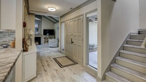 A hallway with a staircase, a television, and a door leading outside. - Sunset Rentals | 5 Rice Lane | Dog Friendly (Hilton Head Island)