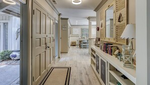 A hallway with a wooden floor, a door on the left, and a bookshelf on the right. - Sunset Rentals | 5 Rice Lane | Dog Friendly (Hilton Head Island)