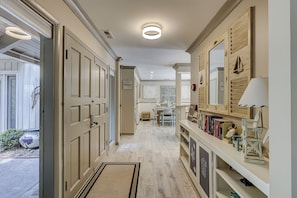 A hallway with a wooden floor, a door on the left, and a bookshelf on the right. - Sunset Rentals | 5 Rice Lane | Dog Friendly (Hilton Head Island)