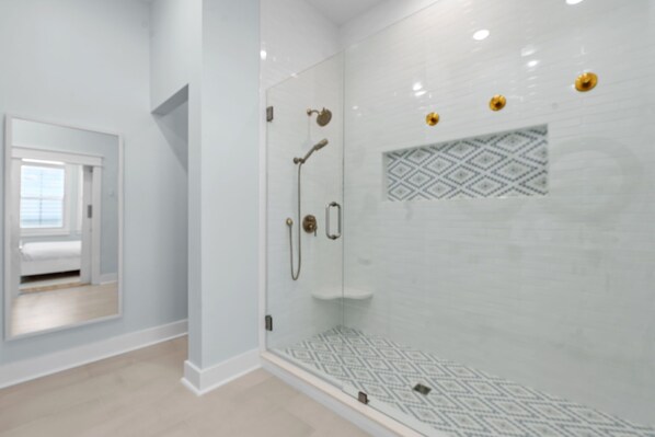 A modern bathroom with a glass shower enclosure, a small sink, and a patterned tile backsplash.