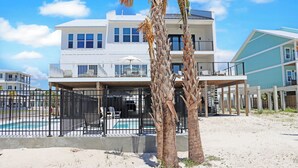 Un edificio de dos pisos con piscina, palmeras y una playa de arena.