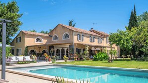Una casa de dos pisos con piscina, mobiliario exterior y jardín.