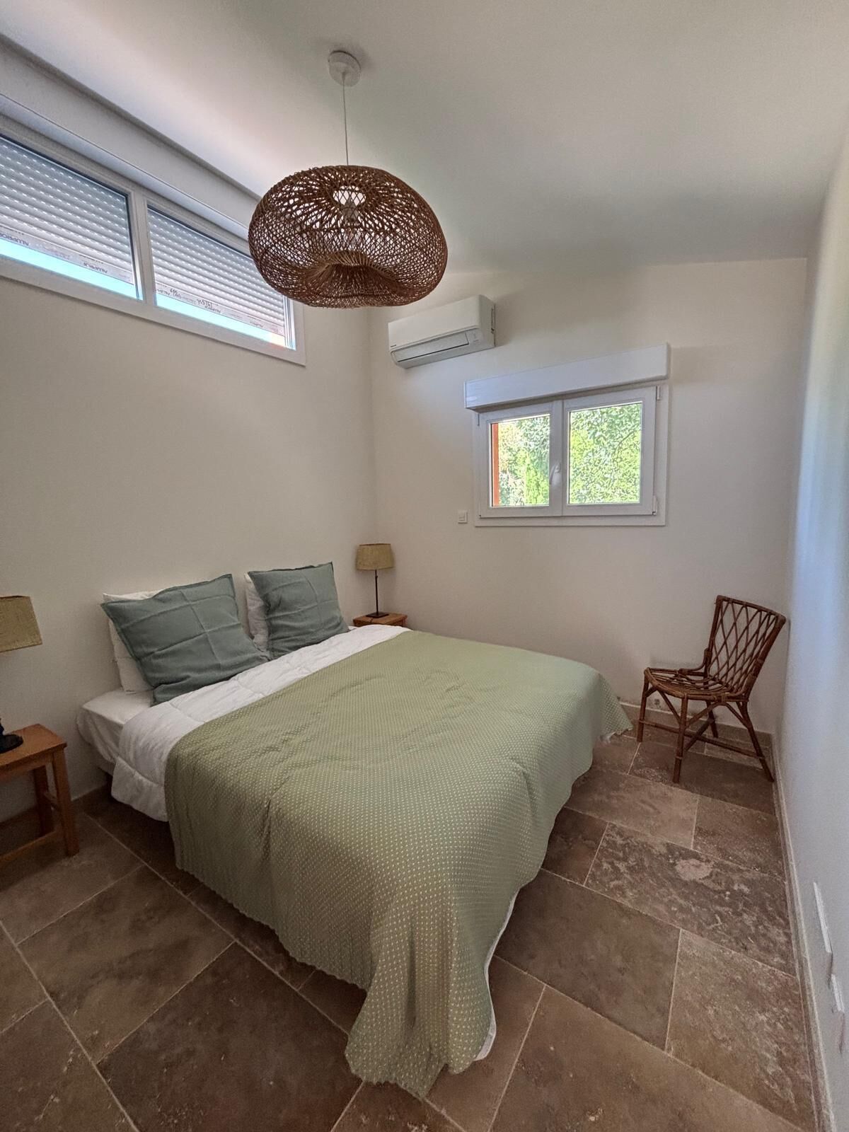 Une chambre à coucher avec un lit, une fenêtre, une chaise, une lampe et un climatiseur.
