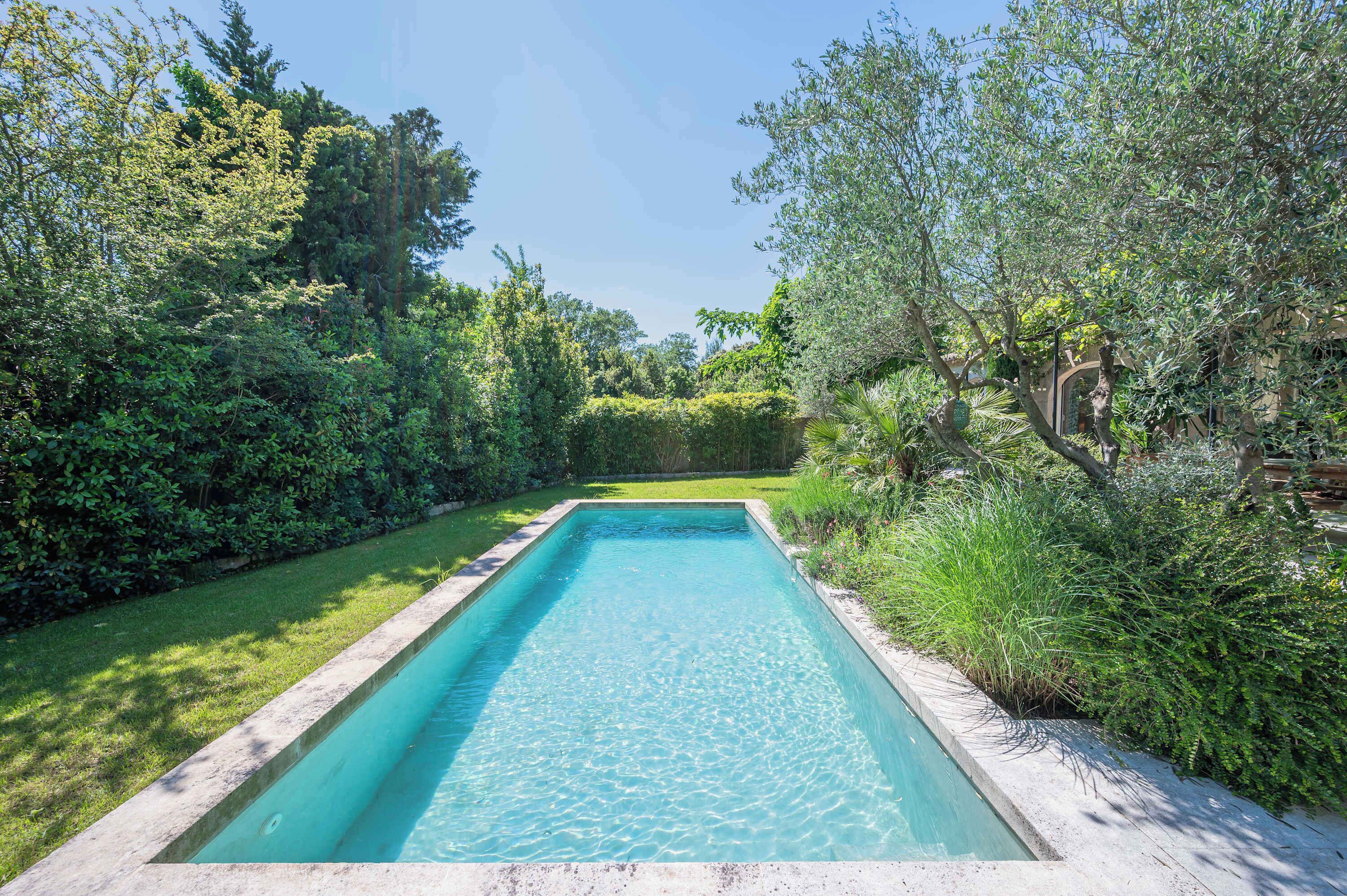 A rectangular swimming pool with clear blue water, surrounded by lush greenery and a well-maintained lawn.