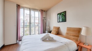 A hotel room with a large bed, a view of the city through the window, a radiator, and a bedside table with a lamp. - Superb T3 near Place des Vosges (Paris)
