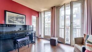 A modern living room with a piano, a sofa, and large windows with curtains. - Superb T3 near Place des Vosges (Paris)