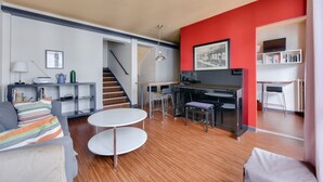 A modern living room with a staircase, a dining area, and a kitchen with red walls. - Superb T3 near Place des Vosges (Paris)