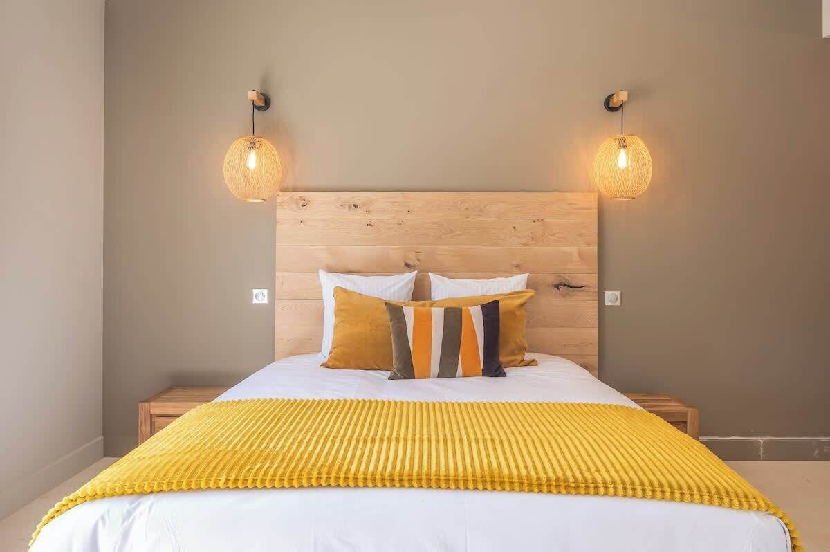 Ein Bett mit hölzernem Kopfteil, zwei Wandlampen und einer gelben Tagesdecke.