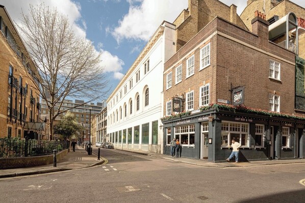 A street view with a pub named "Dean Swift" on the corner, featuring large windows and a signboard advertising craft beer and food.