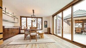 A modern kitchen with wooden cabinets, a dining area with a wooden table and chairs, and large sliding glass doors leading to an outdoor space. - Luxe 4 Bedroom Beaver Creek Lodge Condo With ski in, ski out Access (Avon)