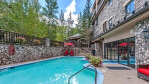 A pool area with stone walls, red lounge chairs, and a staircase leading to a building. - Luxe 4 Bedroom Beaver Creek Lodge Condo With ski in, ski out Access (Avon)