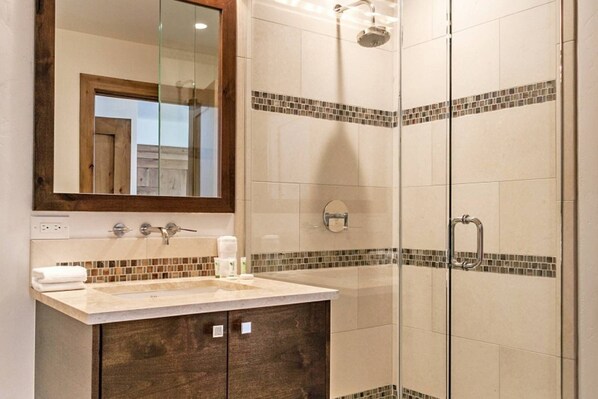A bathroom with a glass-enclosed shower, a vanity with a mirror, and a tiled backsplash.