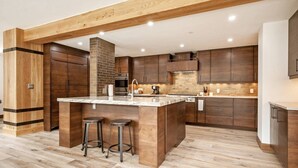 A modern kitchen with wooden cabinetry, a central island with stools, and a brick backsplash. - Luxe 4 Bedroom Beaver Creek Lodge Condo With ski in, ski out Access (Avon)