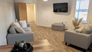 A modern living room with two grey sofas, a wooden coffee table, and a flat-screen TV mounted on the wall. - Ground Floor Apartment - Cloisters Coastal Escape (East Riding of Yorkshire)