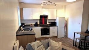 A compact kitchen with white cabinets, a black stove, and a white refrigerator. - Ground Floor Apartment - Cloisters Coastal Escape (East Riding of Yorkshire)