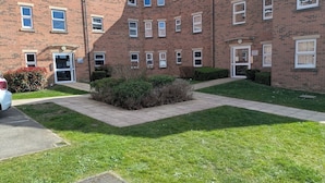 A multi-story brick building with a central courtyard, a car parked in front, and a well-maintained lawn. - Ground Floor Apartment - Cloisters Coastal Escape (East Riding of Yorkshire)