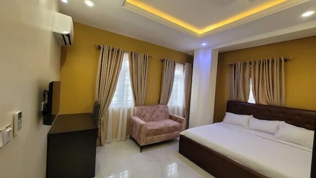 A hotel room with a bed, a chair, a desk, and a TV. - Riverview Hotel and Suites (Ife)