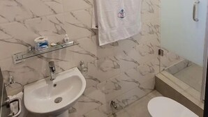 A bathroom with a marble-patterned wall, a sink, a toilet, and a glass shower enclosure. - Riverview Hotel and Suites (Ife)