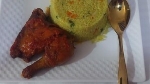 A plate with a mound of yellow rice, two pieces of grilled chicken, and a spoon. - Riverview Hotel and Suites (Ife)