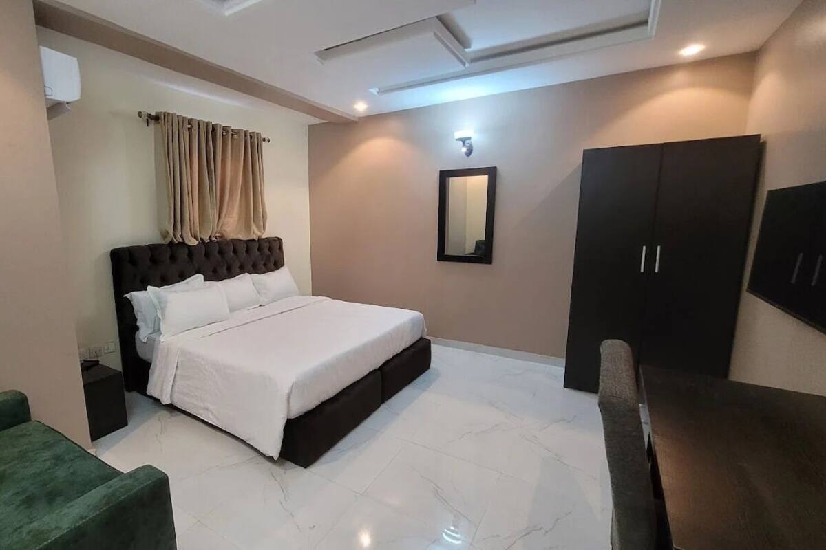 A bedroom with a bed, a green armchair, a wardrobe, and a mirror on the wall.