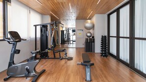 Ein Fitnessraum mit Trainingsgeräten, Holzböden und großen Fenstern.