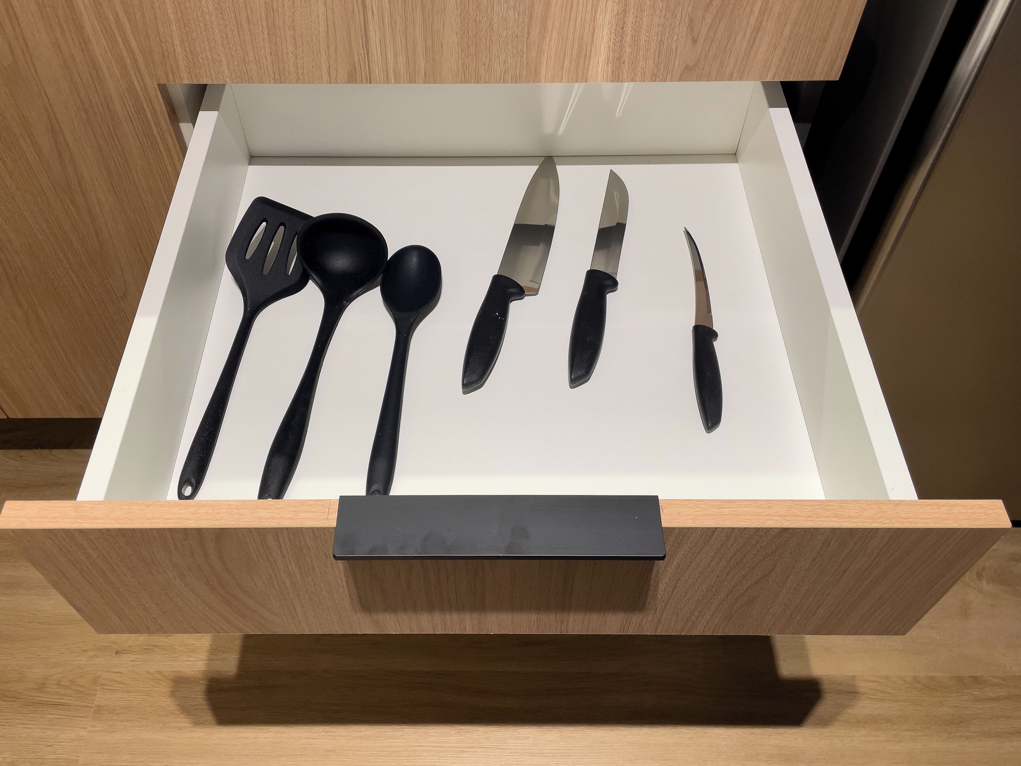 A drawer with kitchen utensils including a spatula, ladle, and knives.