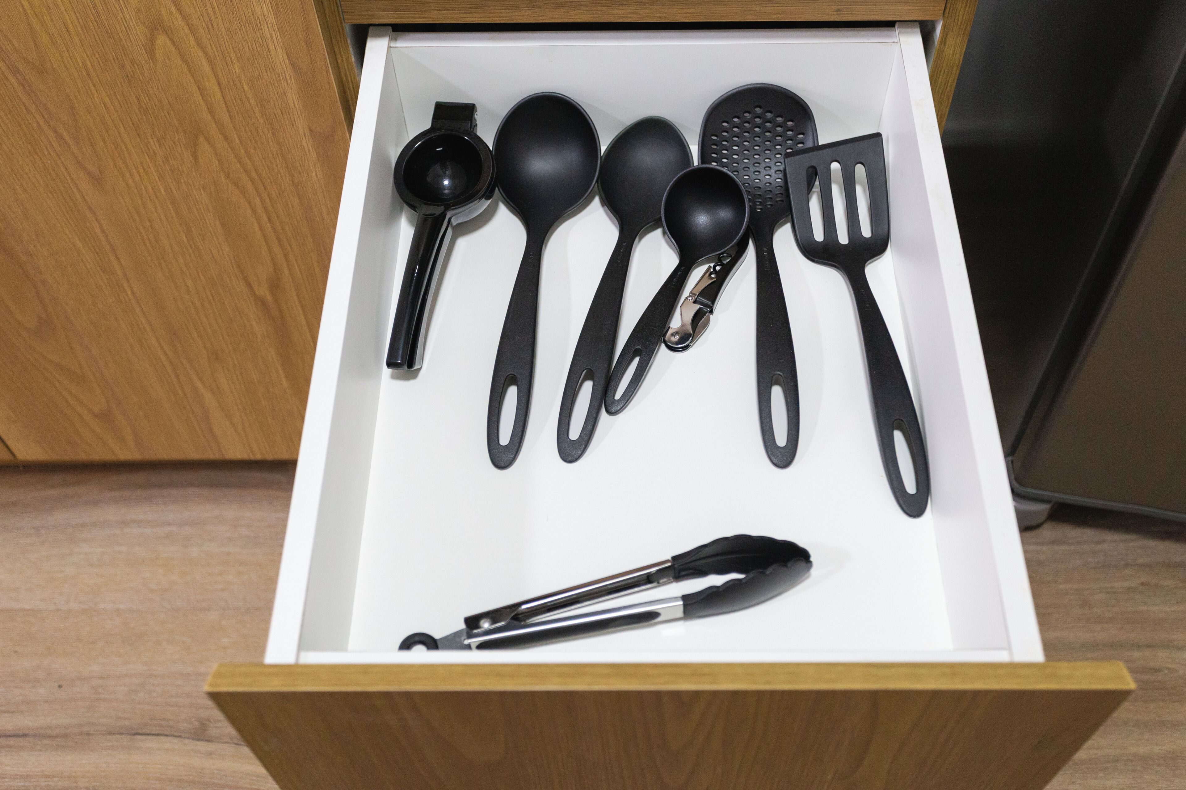 A drawer with black kitchen utensils including a ladle, spoon, spatula, and tongs.