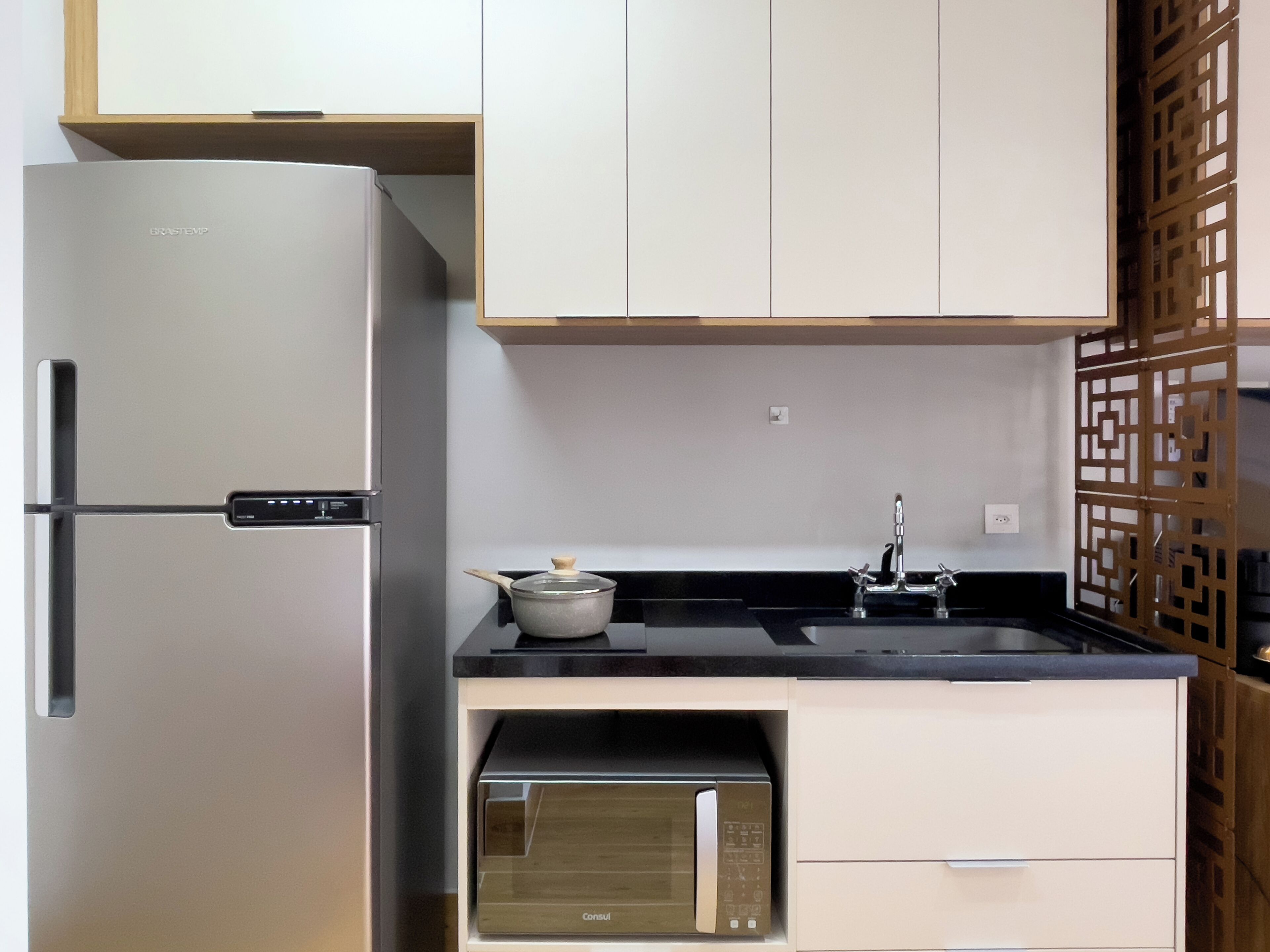 A kitchen with a stainless steel refrigerator, a microwave, a sink, and wooden cabinets.