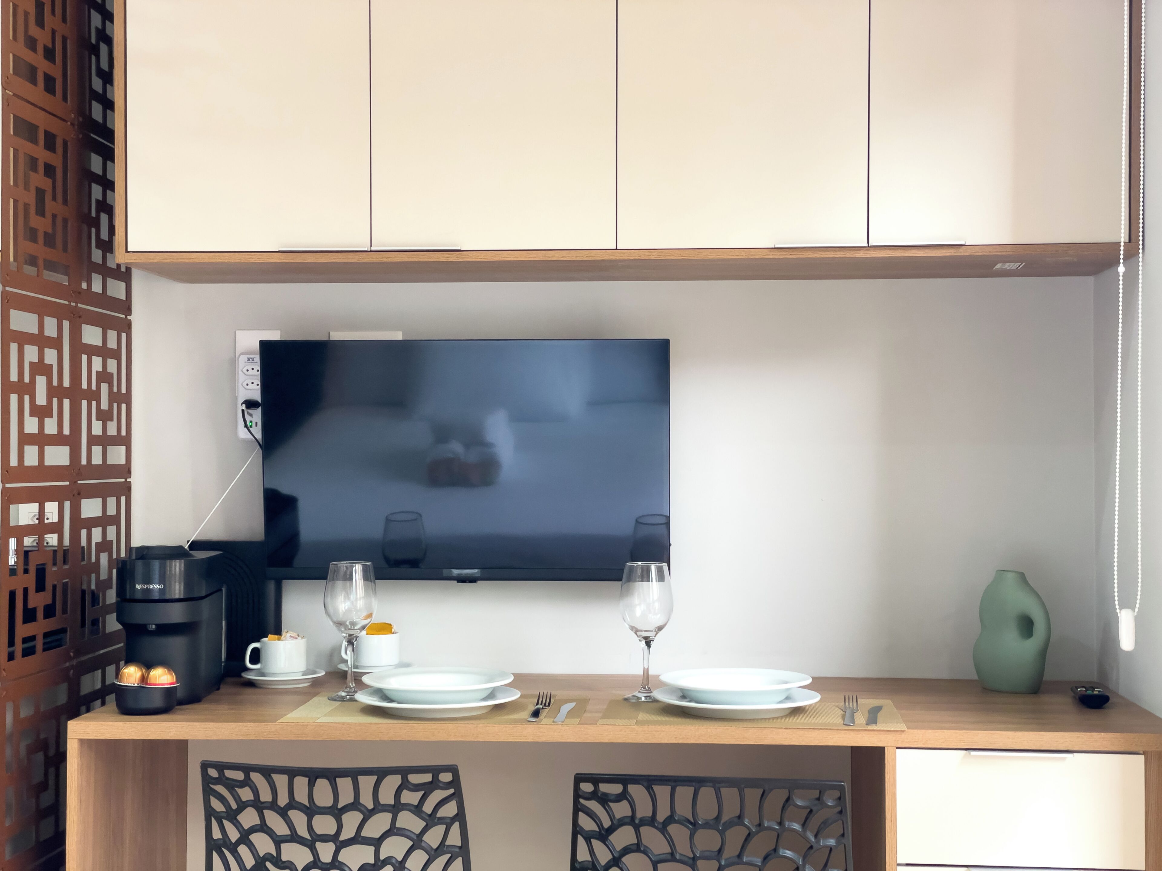 Una kitchenette con cafetera, dos vasos, un plato y un televisor fijado a la pared.