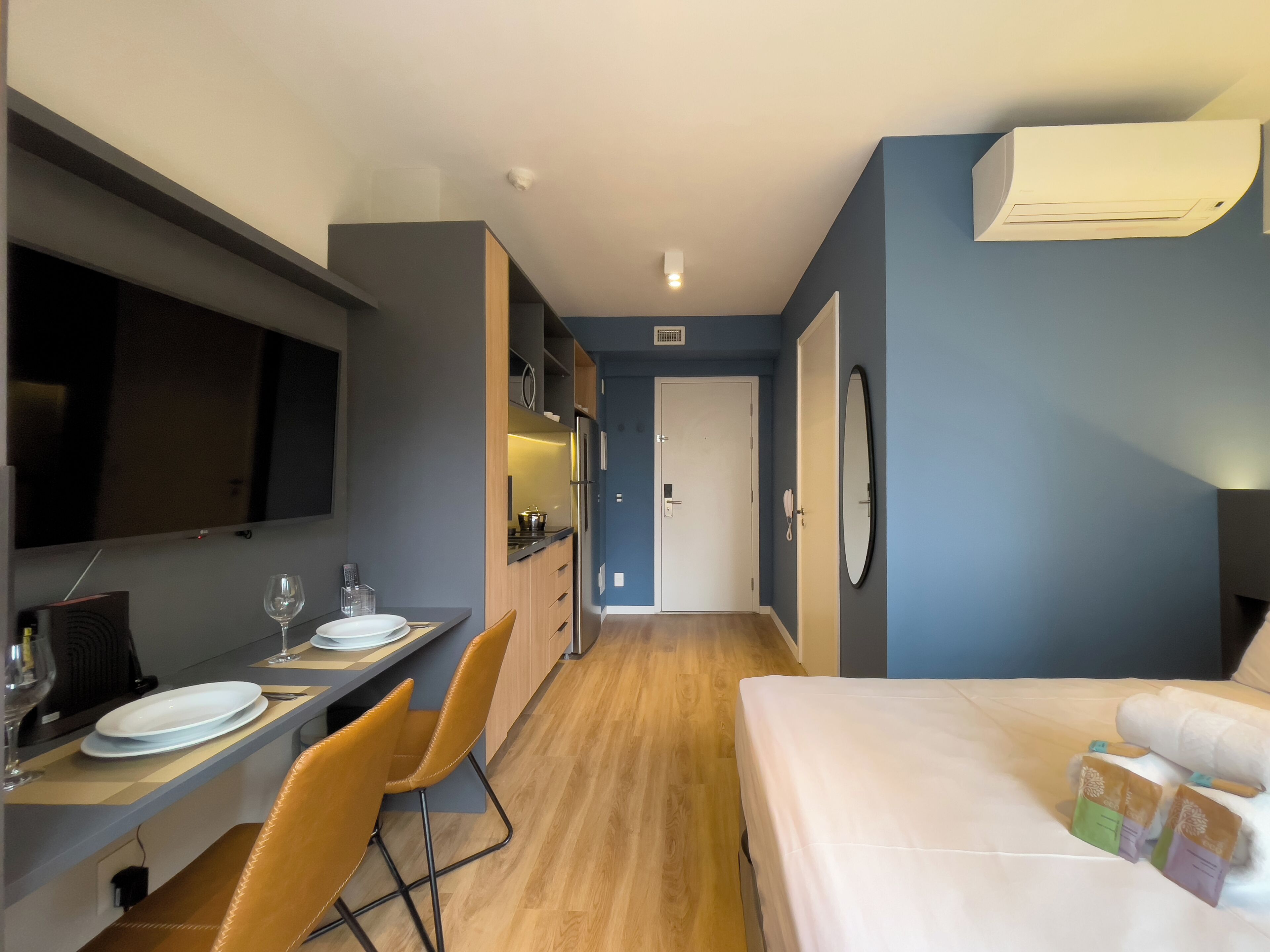 Kompakti hotellihuone, jossa on pieni keittiö, ruokailutila, sänky ja kylpyhuone.