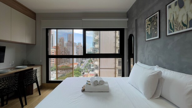 Ein Hotelzimmer mit Bett, Schreibtisch, Stuhl, Fenster mit Blick auf Gebäude und Kunstwerken an der Wand.