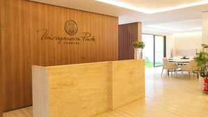 Ein Empfangsbereich mit einem Holzbüro, einem Logo und Blick auf einen Essbereich mit Tisch und Stühlen.